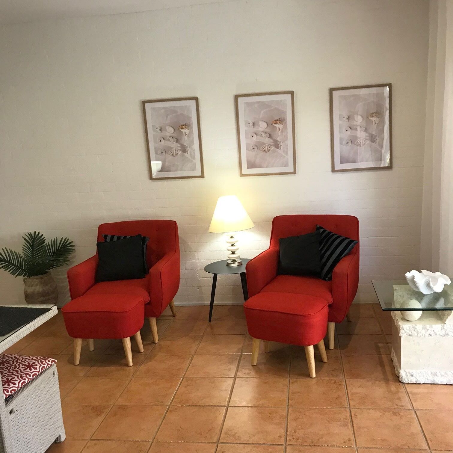 Un salón con dos sillones rojos, una mesita de noche con una lámpara y tres cuadros enmarcados en la pared.