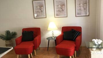 Un salón con dos sillones rojos, una mesita de noche con una lámpara y tres cuadros enmarcados en la pared.