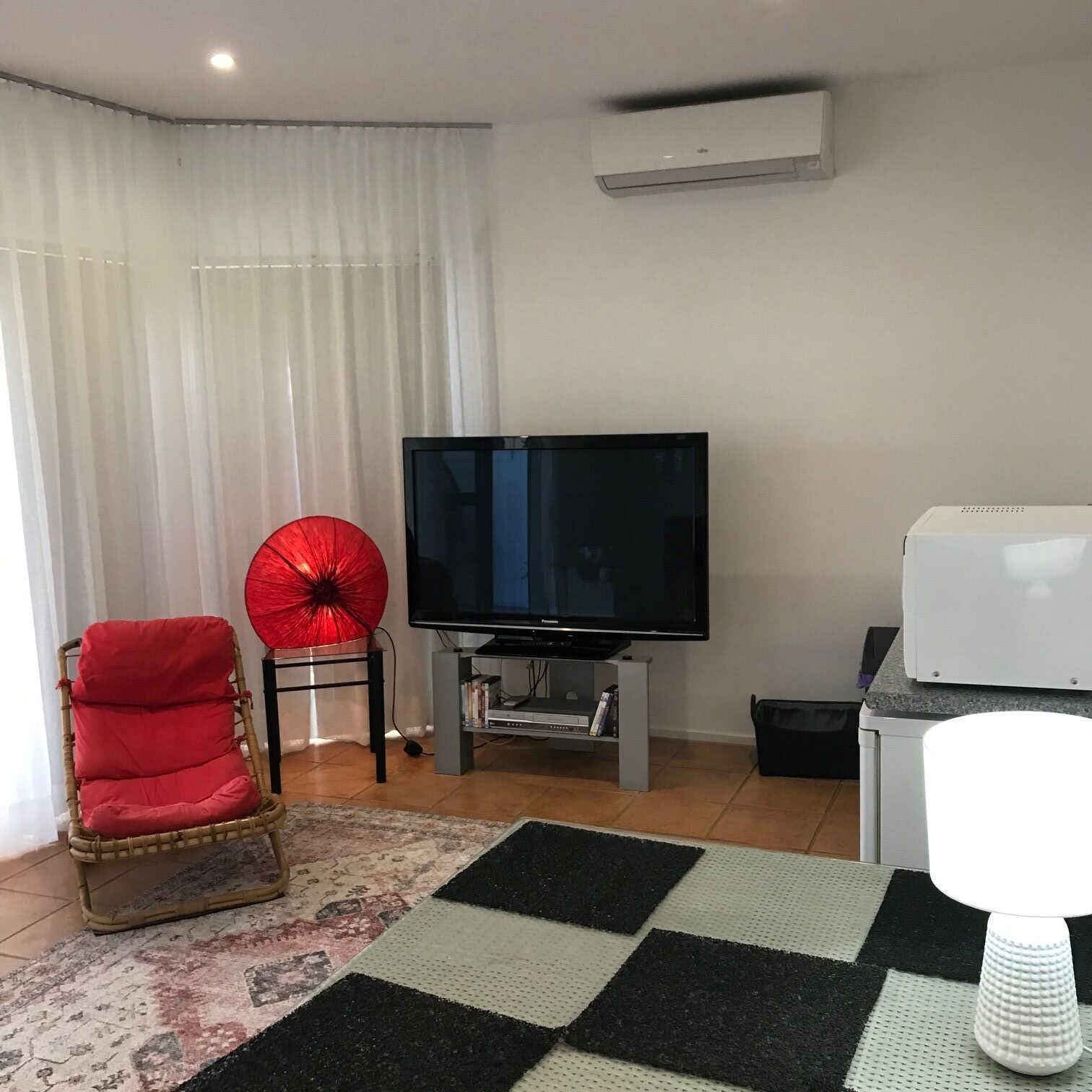 Ein Wohnzimmer mit Flachbildfernseher, einem roten Sessel, einem roten Regenschirm und einem weißen Kühlschrank.
