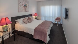 Une chambre à coucher bien rangée, avec un lit, des lampes de chevet, une chaise, un téléviseur et un ventilateur de plafond.