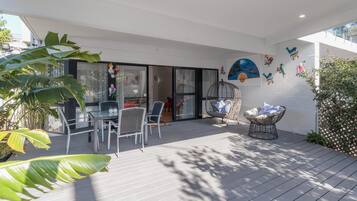 A patio with a dining table and chairs, a wicker chair, and a decorative wall with bird and flower art.