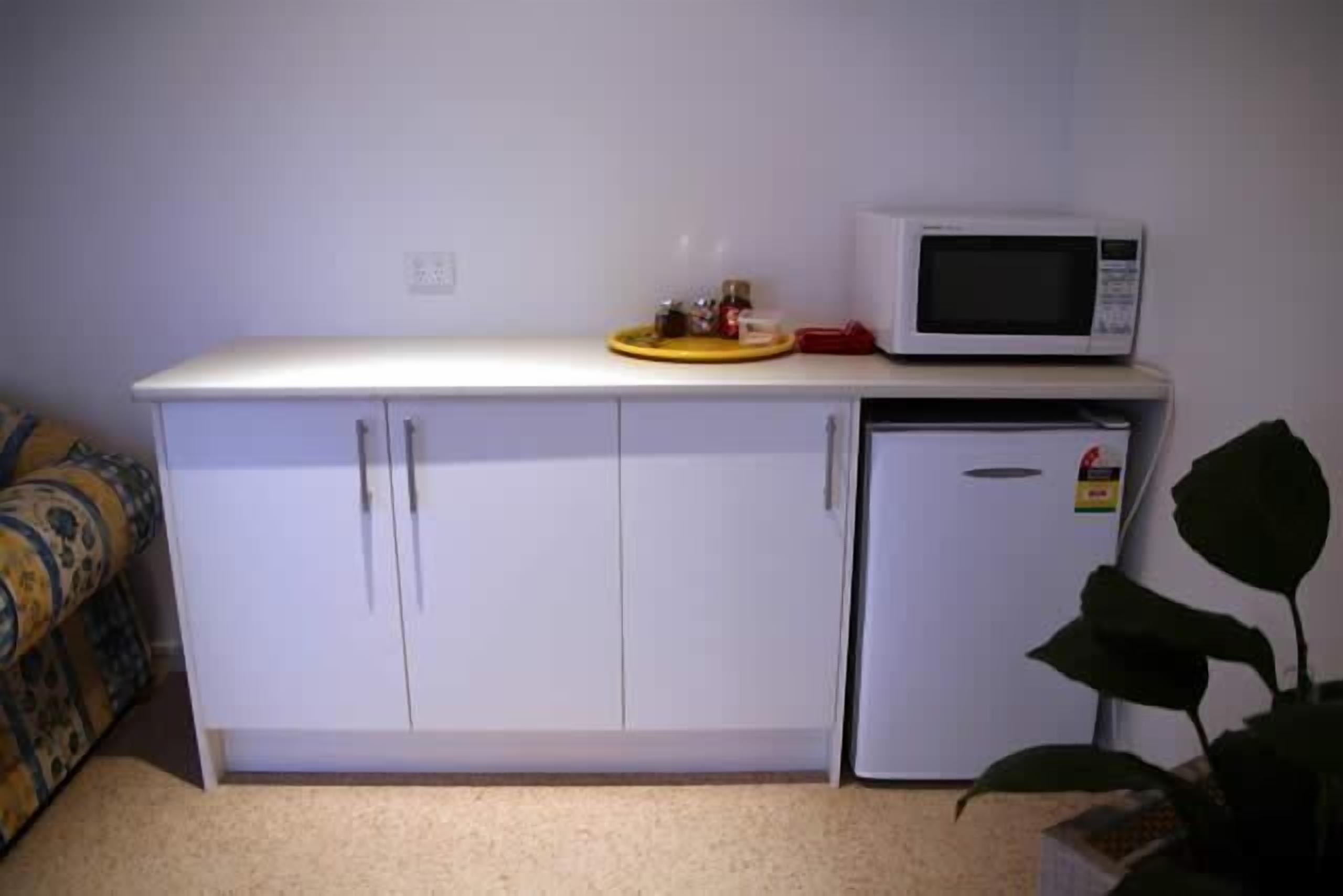 Una kitchenette compacta con microondas, un refrigerador pequeño y una encimera con una bandeja y frascos.
