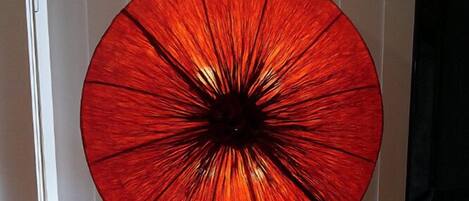 A red glass object on a black metal stand in a room with tiled flooring.