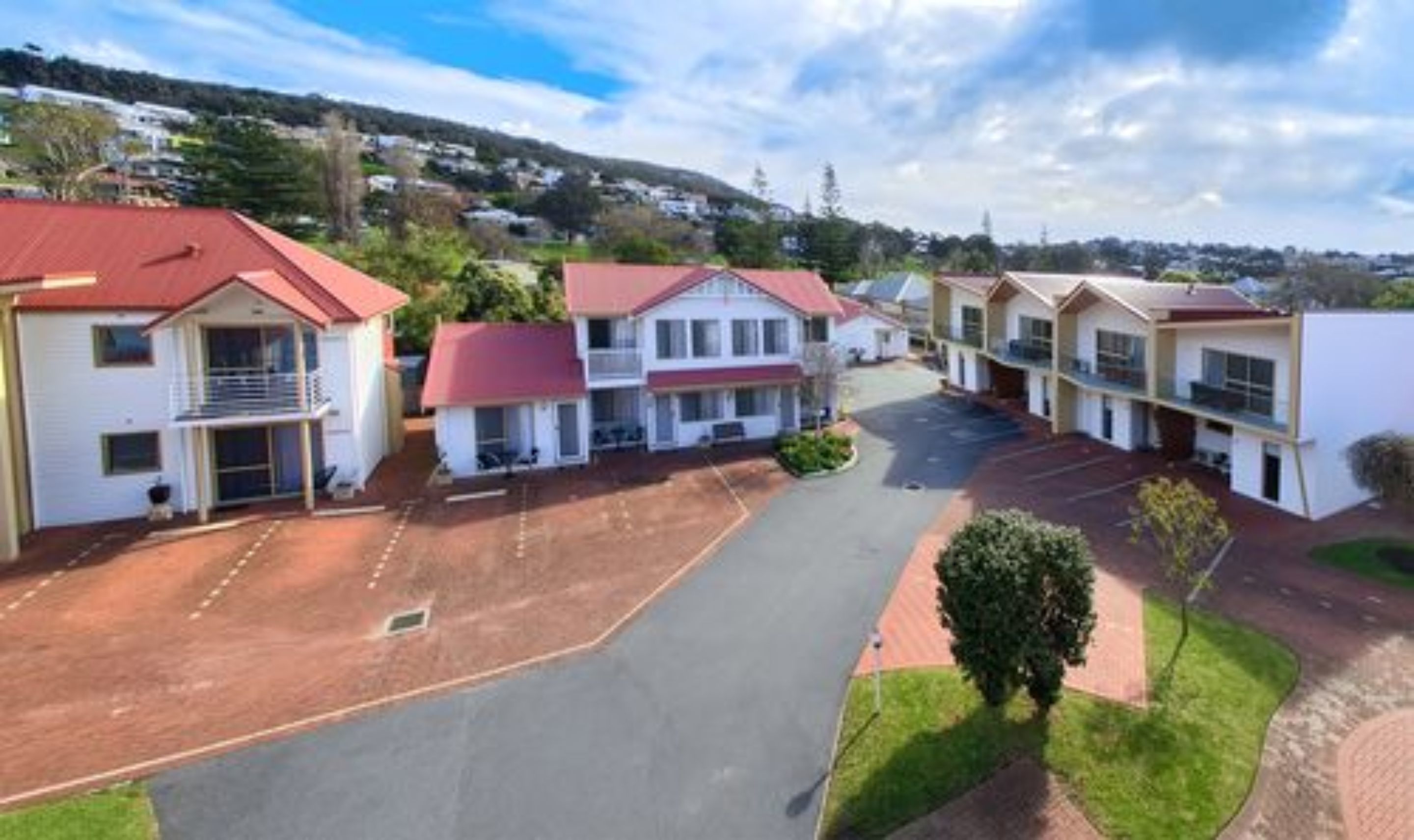 A row of single-story buildings with red roofs, arranged in a linear fashion with a central paved area.