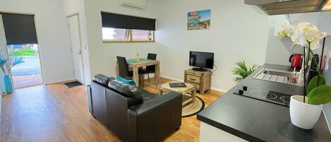 A modern living room with a sofa, TV, dining table, and kitchen area.