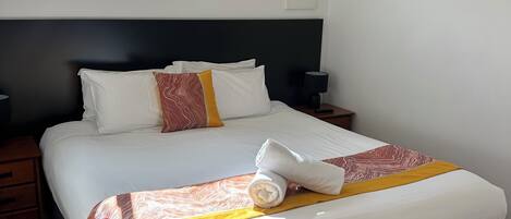 A neatly made bed with a rolled towel, a bedside table with a lamp, and a window with a view of trees.