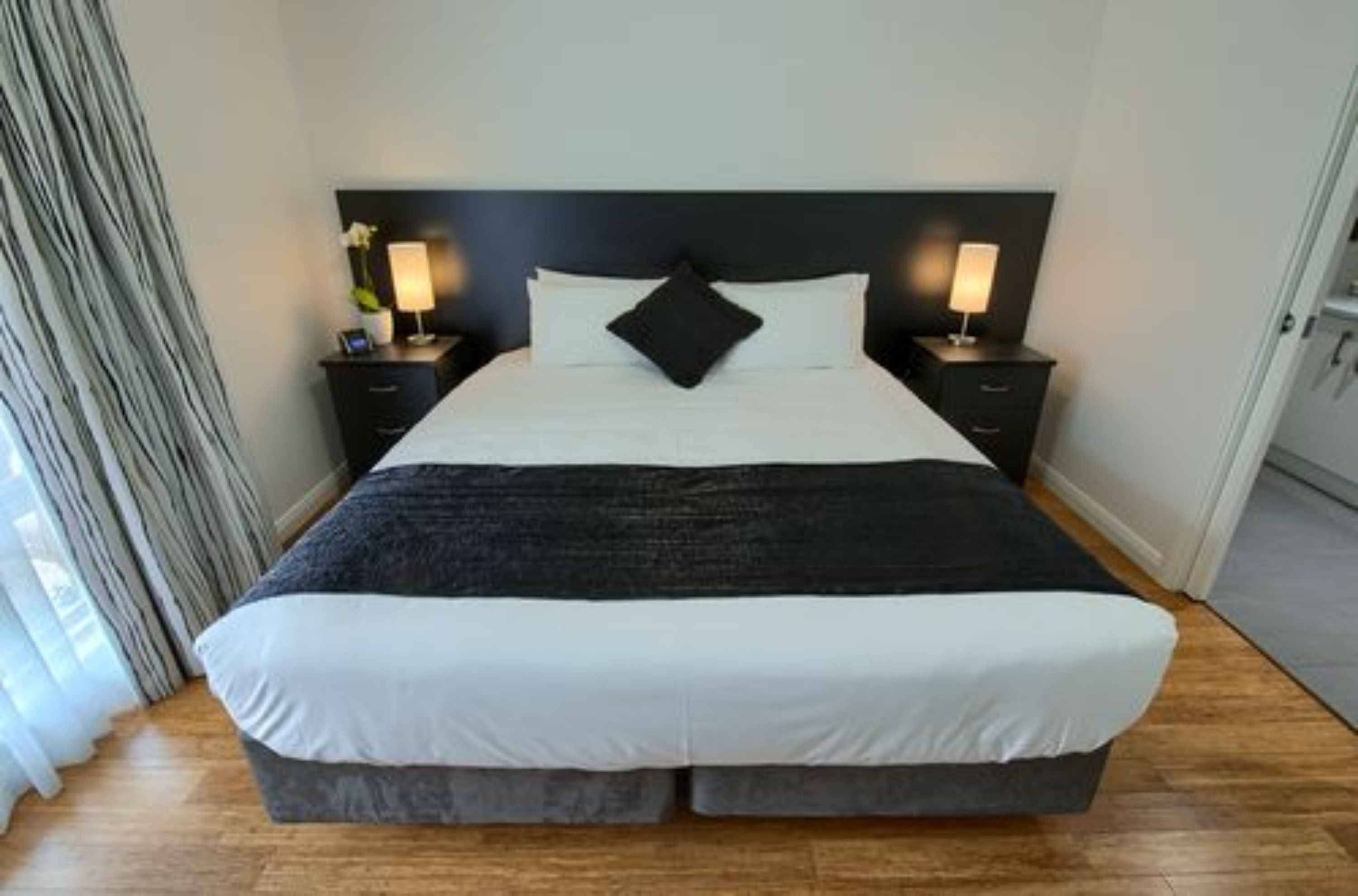A neatly made bed with white and black bedding, two bedside tables with lamps, and a dark headboard.
