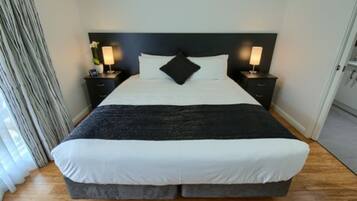A neatly made bed with white and black bedding, two bedside tables with lamps, and a dark headboard.