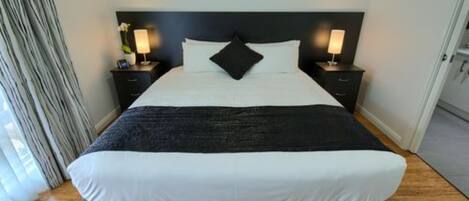 A neatly made bed with white and black bedding, two bedside tables with lamps, and a dark headboard.