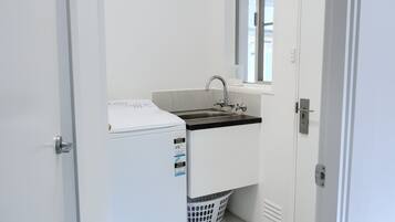 Pequeña lavandería con lavadora, lavabo y ventana.
