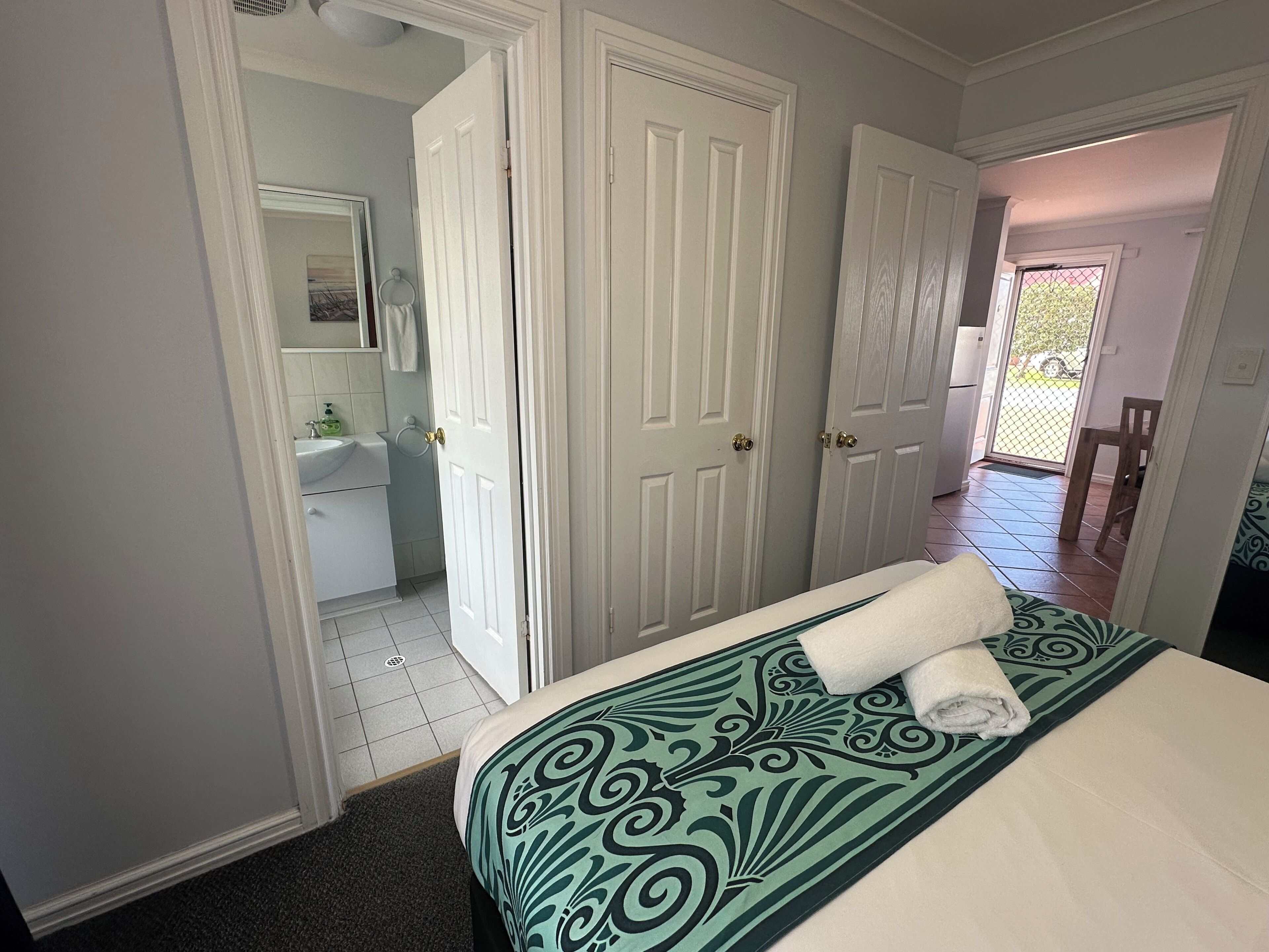 A bedroom with a bed, a bathroom with a sink and mirror, and a door leading to an outdoor area.