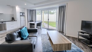 A modern living room with a sofa, coffee table, TV, and a sliding glass door leading to a patio.