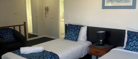A hotel room with two beds, a bedside table with a lamp, a mirror, and a framed picture on the wall.