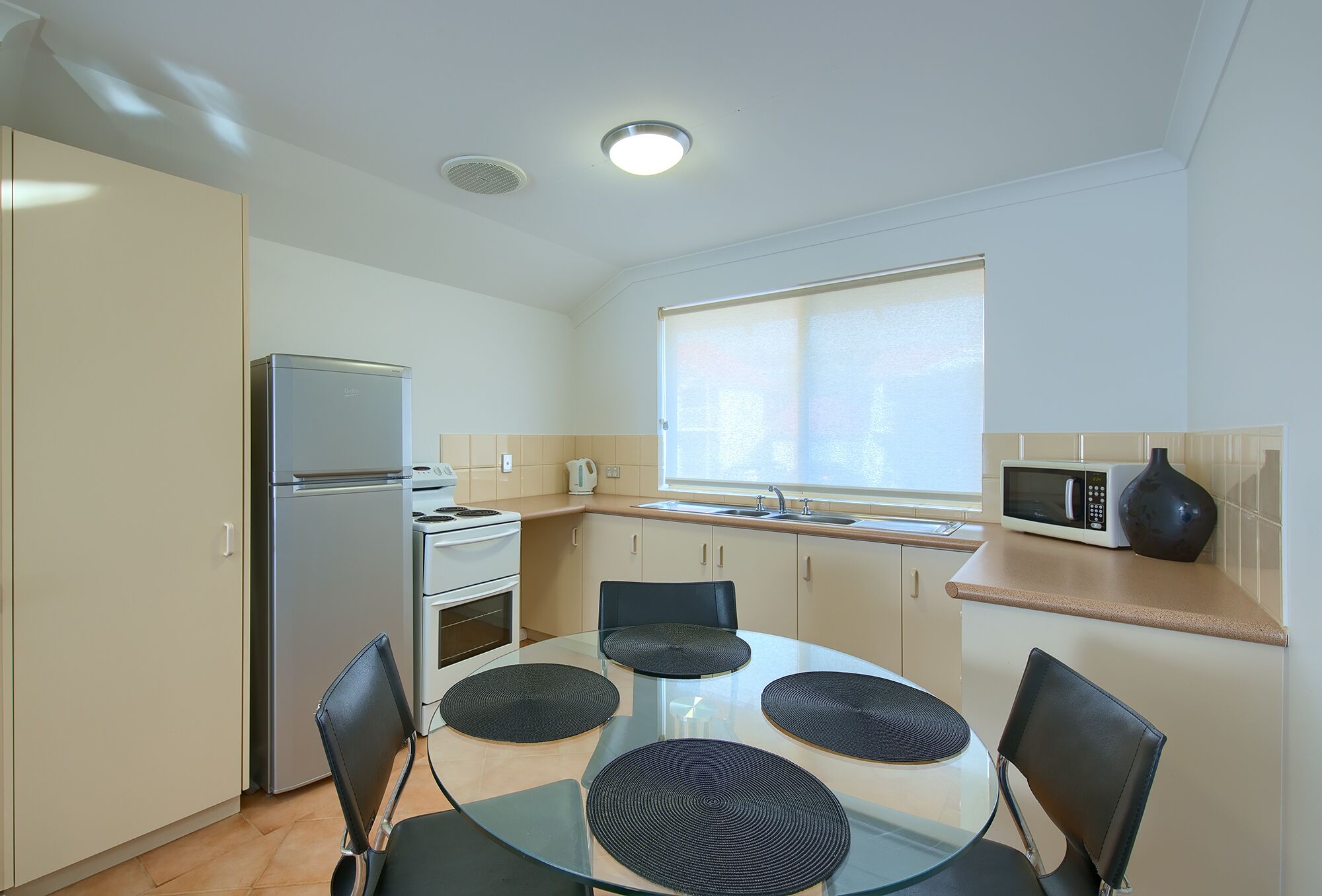 A compact kitchen with a refrigerator, microwave, and stove. There is a window providing natural light and a sink.