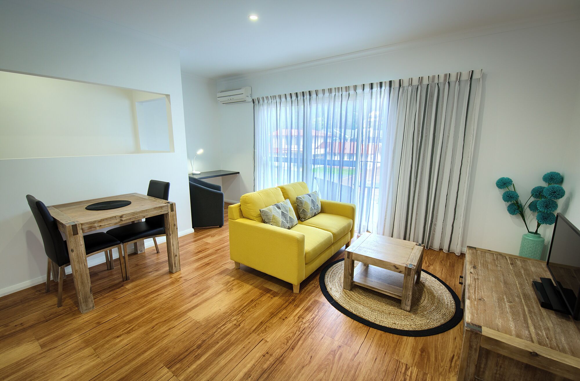 A furnished living room with a wooden dining table, yellow sofa, and a small coffee table.