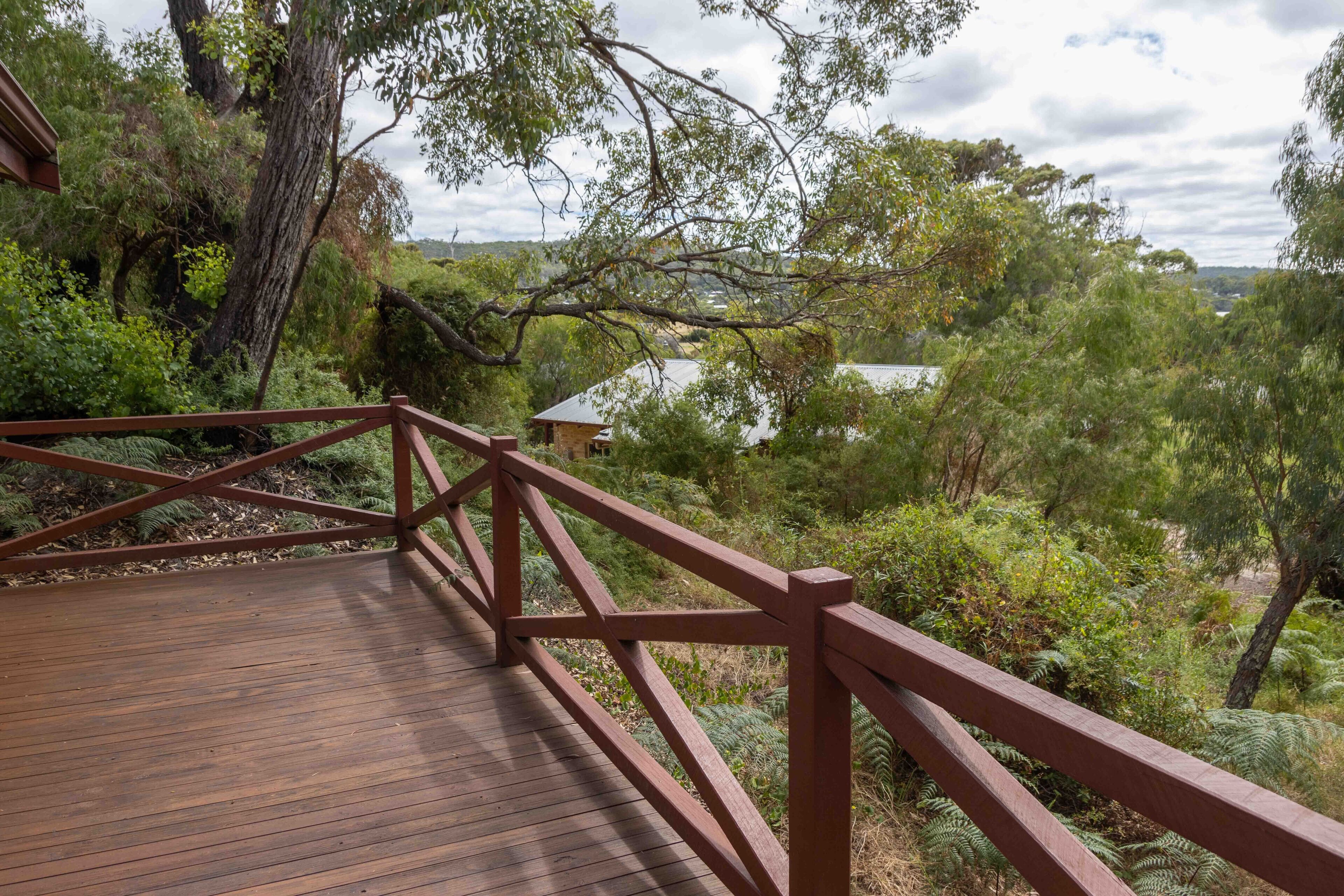 A wooden deck with a railing overlooking a natural landscape with trees and a body of water in the distance.