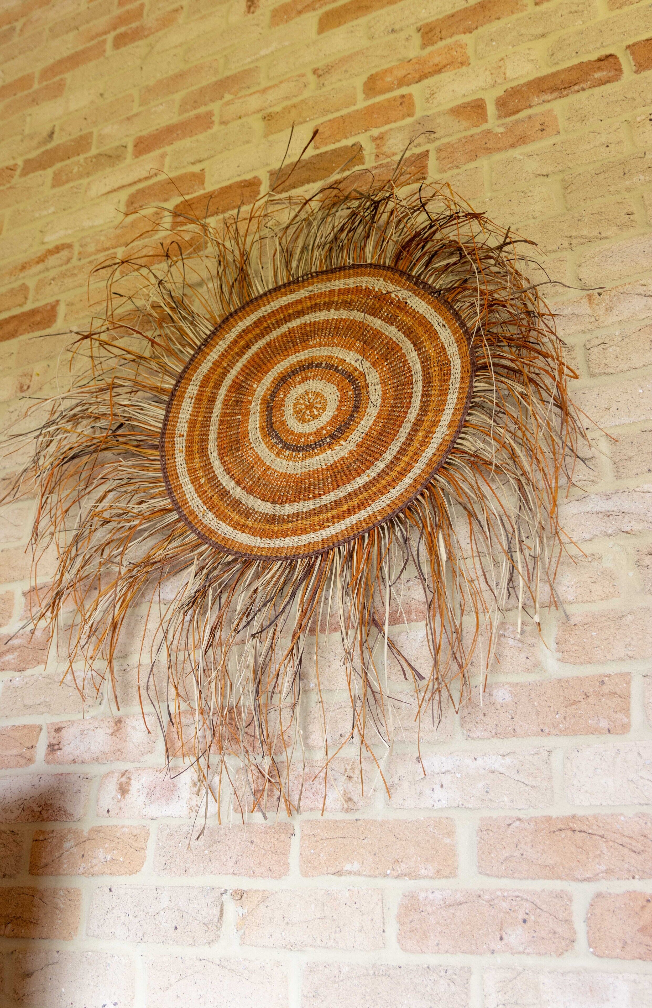 A woven basket with a circular pattern, hanging on a brick wall.