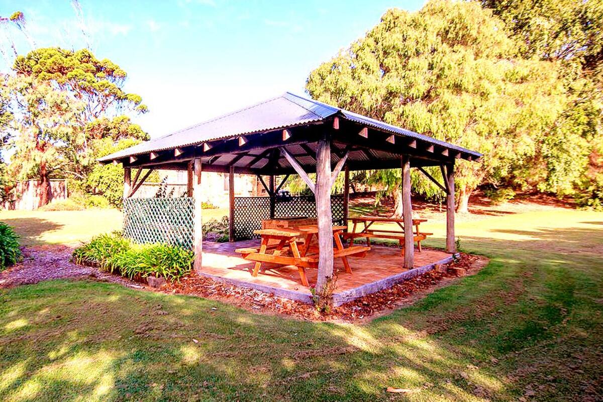 A wooden pavilion with a roof, surrounded by grass and trees.