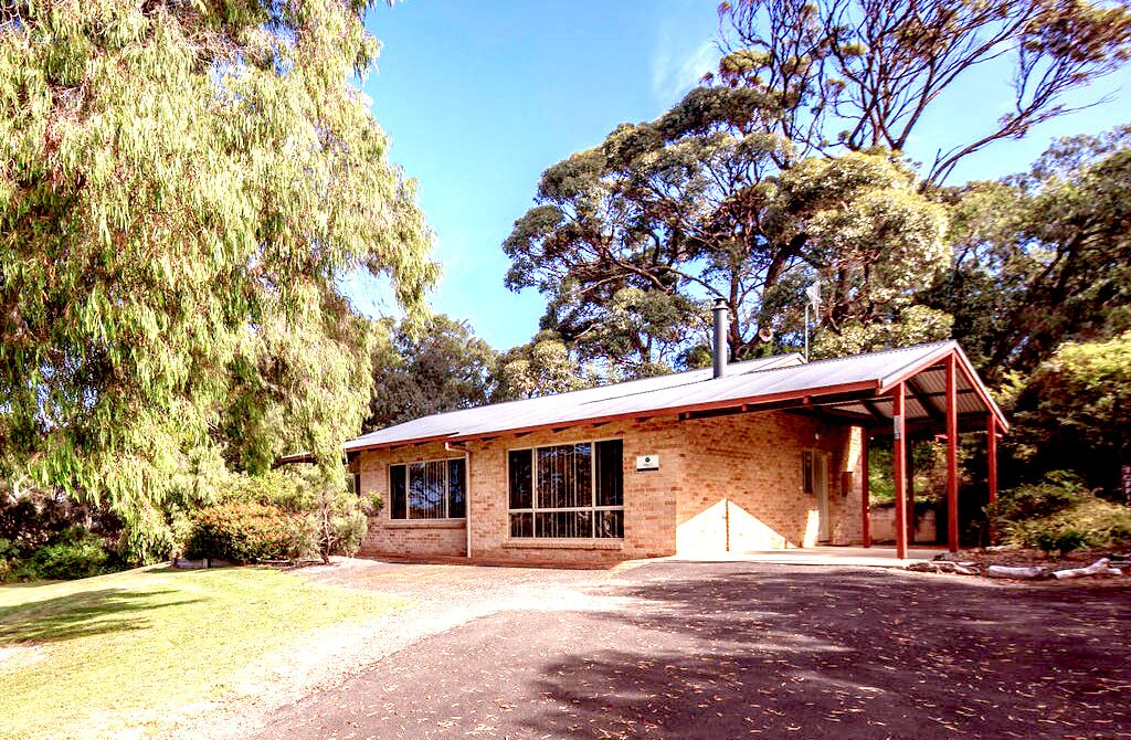 A small brick building with a covered porch and large windows, surrounded by trees.