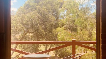 Terraza de madera con mesa y sillas, con vista a un área boscosa.