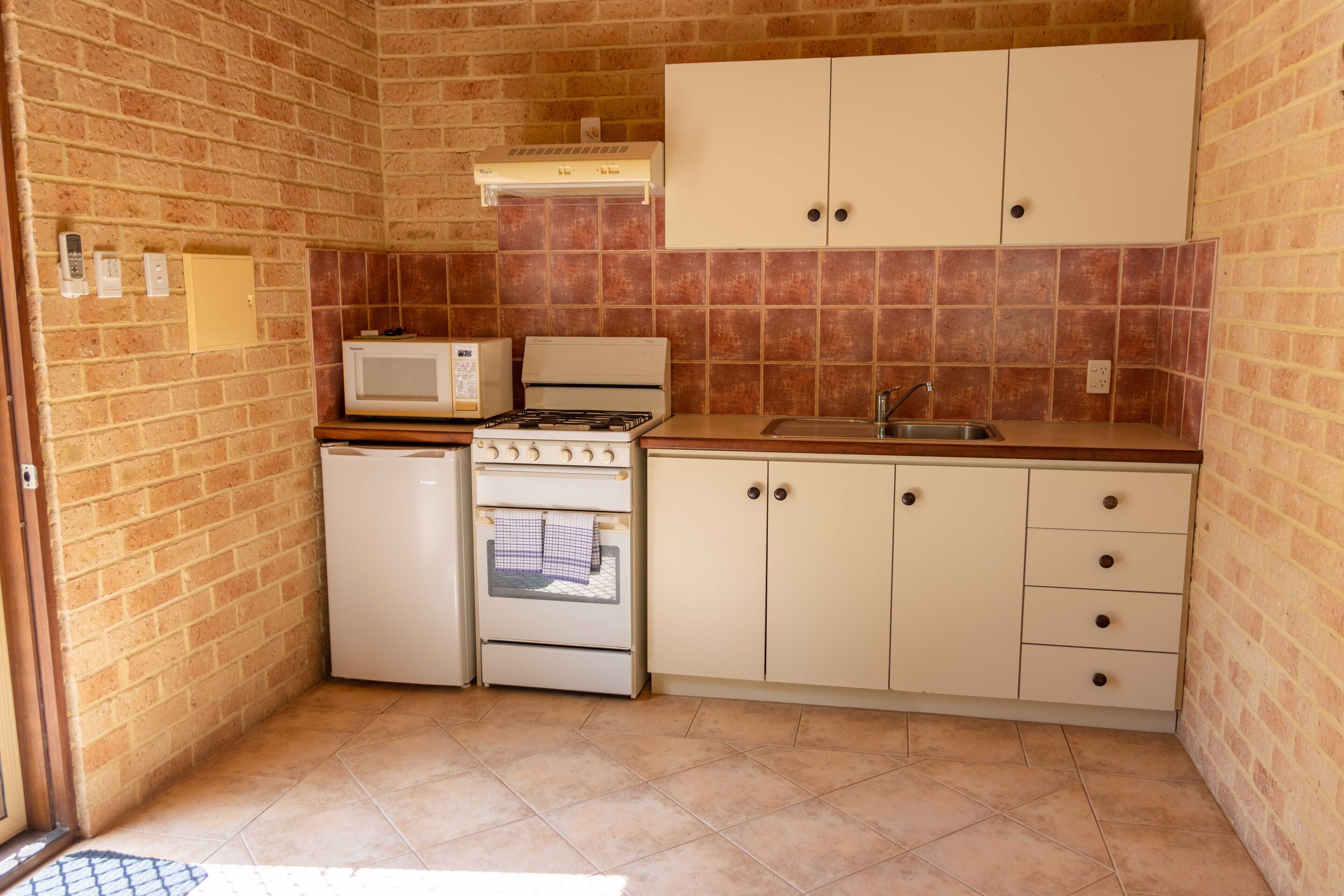 Una cocina compacta con microondas, estufa, horno y armarios blancos.