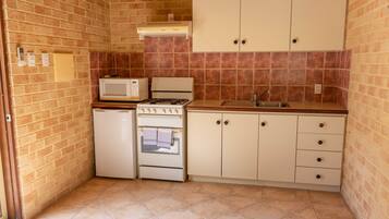 Una cocina compacta con microondas, estufa, horno y armarios blancos.