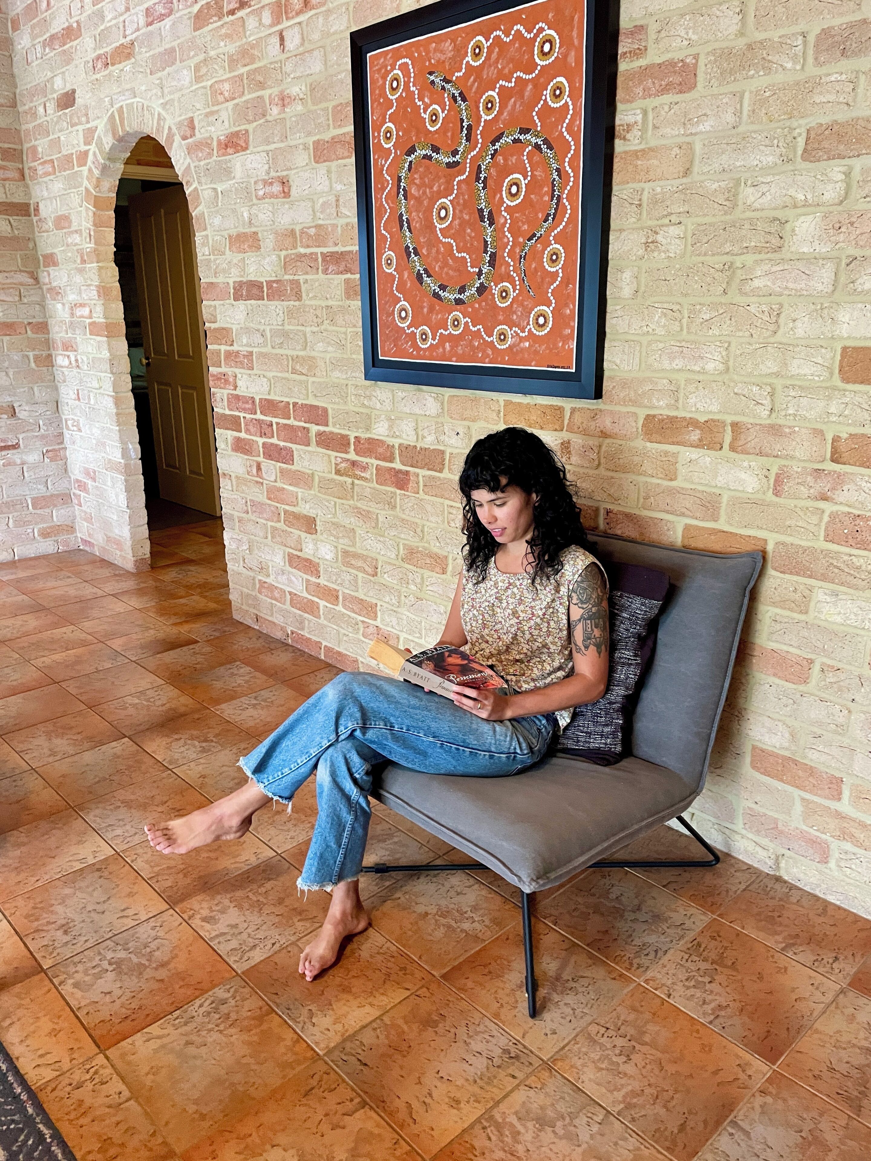 A person sitting on a grey sofa in a room with a brick wall and a tiled floor.