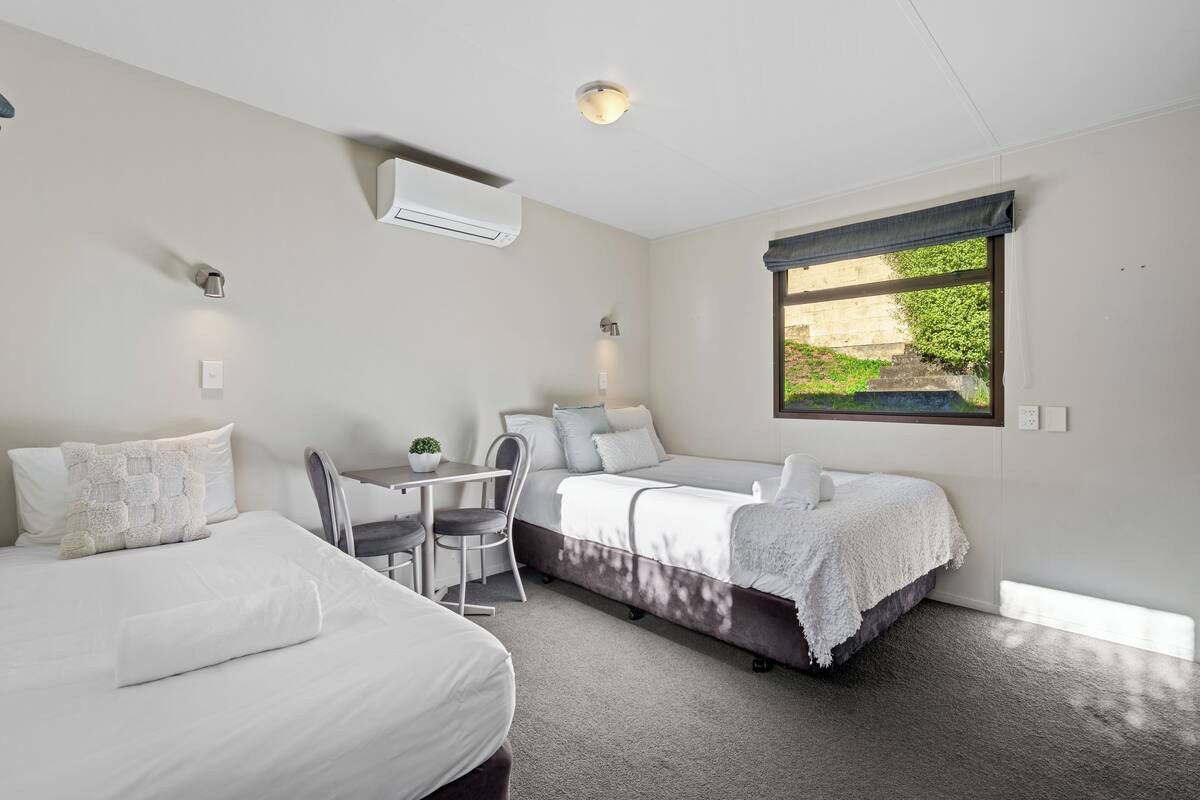 Moderni hotellihuone, jossa on kaksi sänkyä, työpöytä ja tuoli.