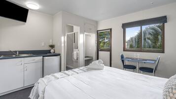 A hotel room with a bed, a desk, a chair, a TV, a shower, and a window.