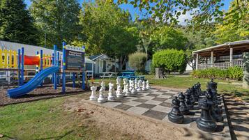 A playground with a slide and climbing structures, a chessboard with oversized chess pieces, and a picnic area with benches.