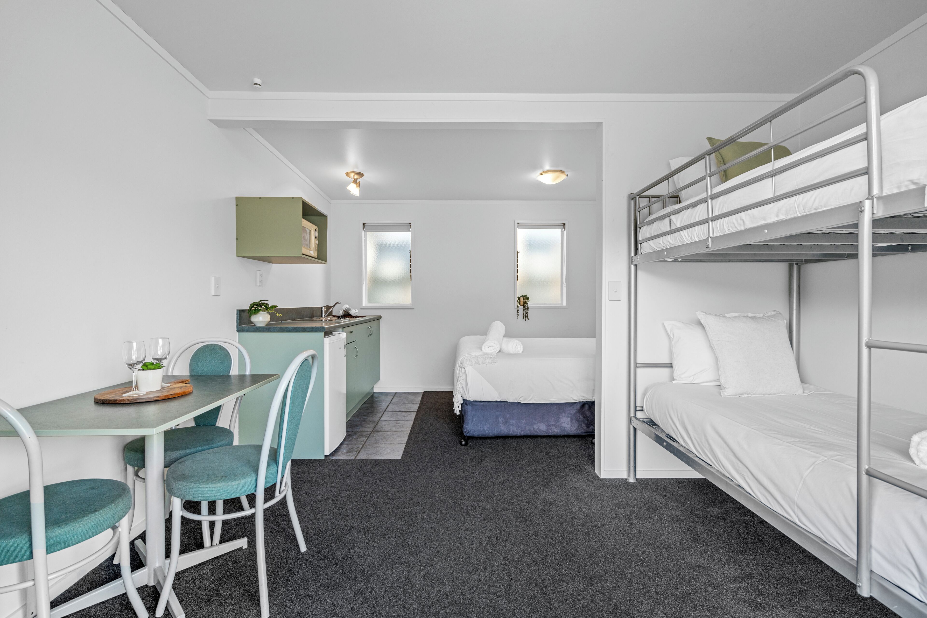 A compact room with bunk beds, a small kitchenette, a dining area, and a single bed.