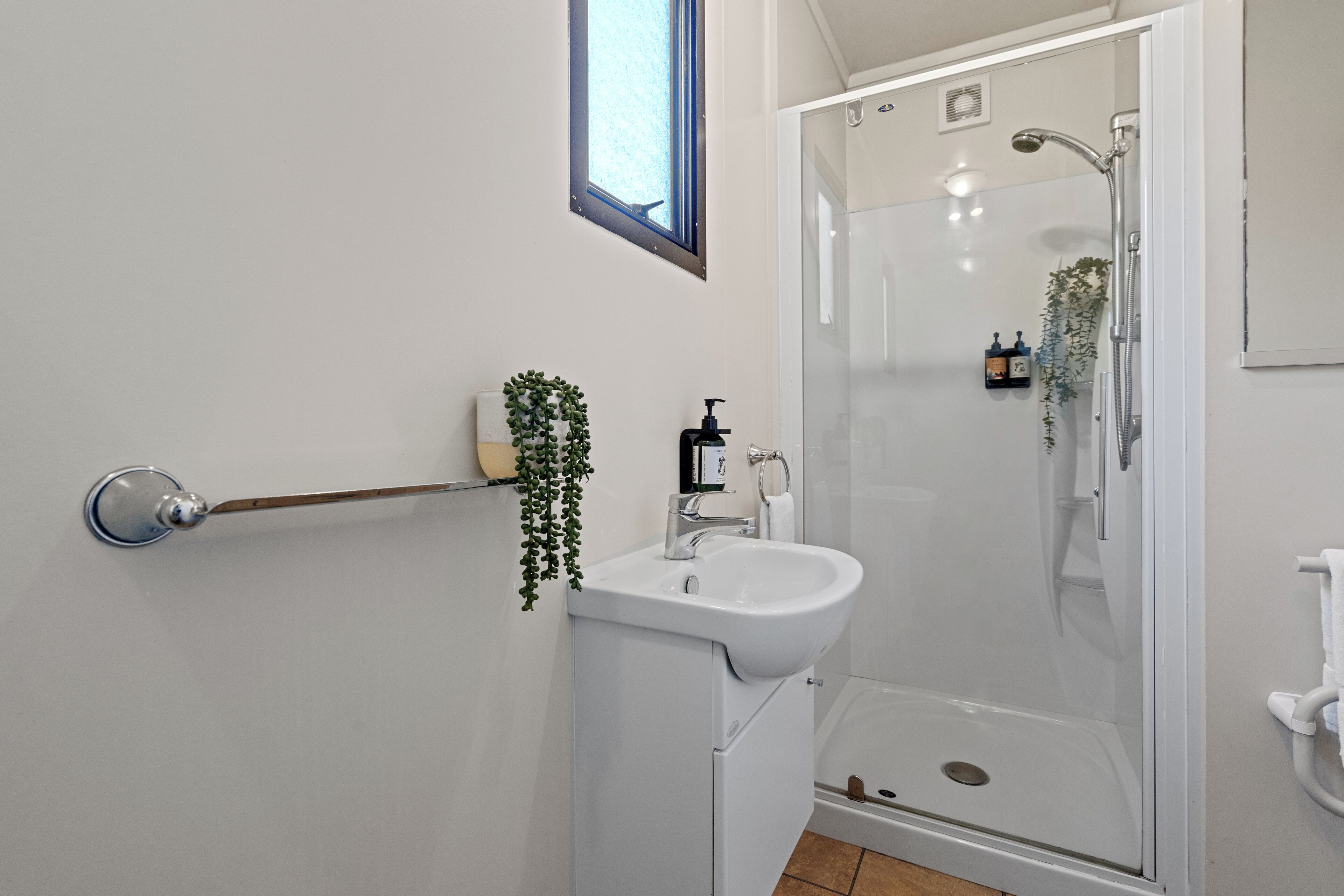 Une salle de bain moderne avec une douche à parois de verre, un lavabo blanc et un porte-serviettes en bois.