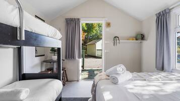 Habitación con literas, una mesita, una silla y un ventanal con cortinas.