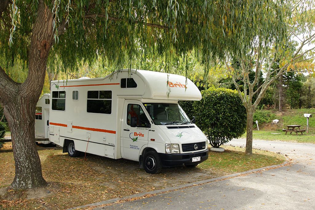 A white RV with the brand name 'Britz' parked under a tree.