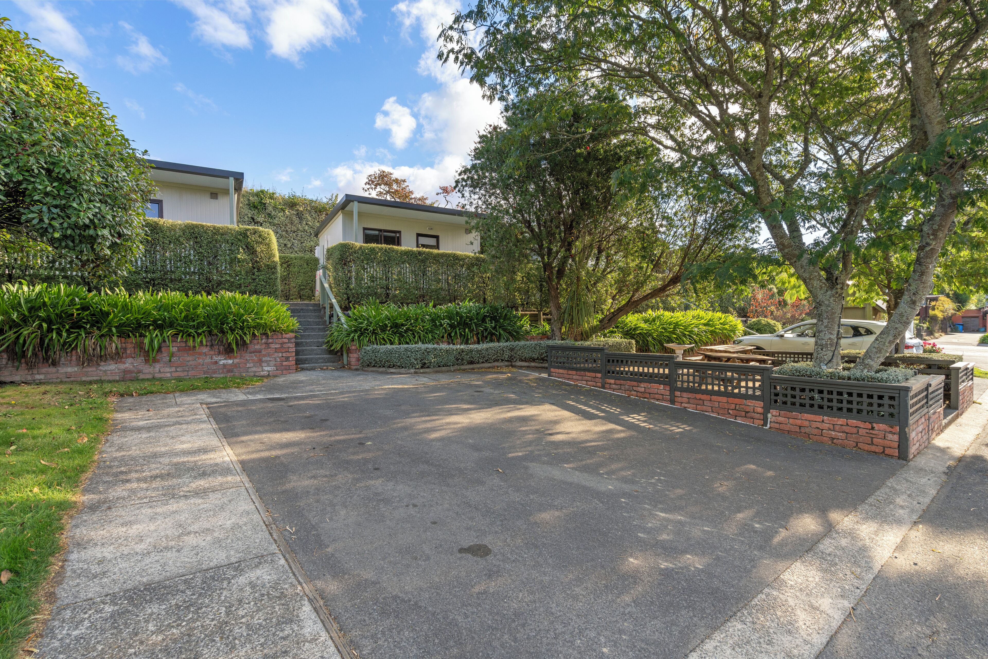 A residential driveway with a hedge, a brick wall, and a tree.