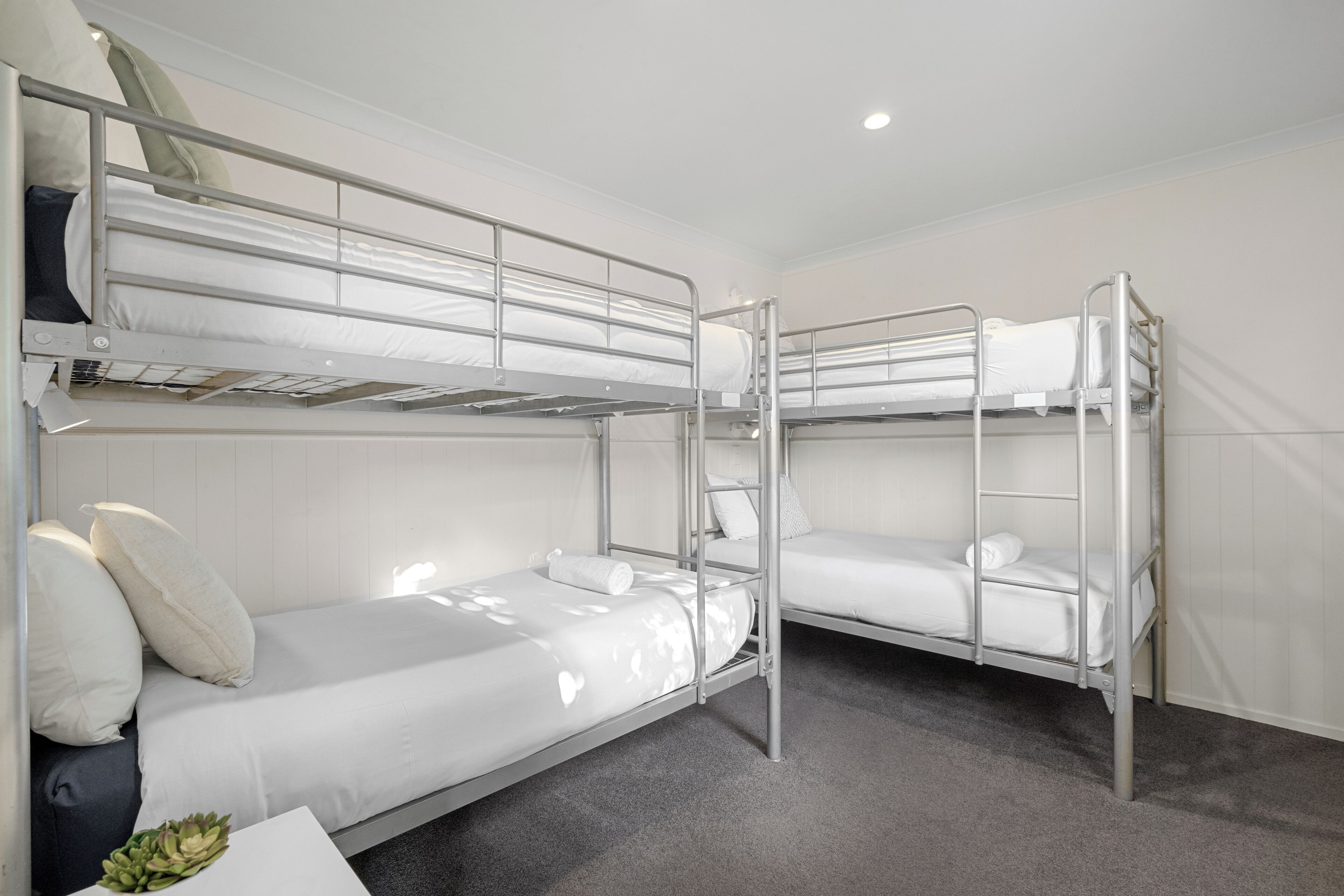 Habitación con literas, ropa de cama blanca y una pequeña mesa con una planta.
