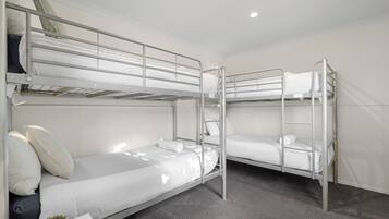 Habitación con literas, ropa de cama blanca y una pequeña mesa con una planta.