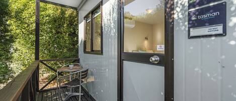 Terraza de madera con mesa y sillas, puerta de cristal y carteles que indican cabañas tipo estudio con baño privado y un cartel de 'No molestar'.