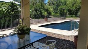 A patio with a pool, surrounded by a fence and greenery.
