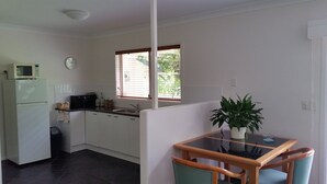 A compact kitchen with white cabinets, a microwave, and a sink. There's a small dining table with chairs and a potted plant.