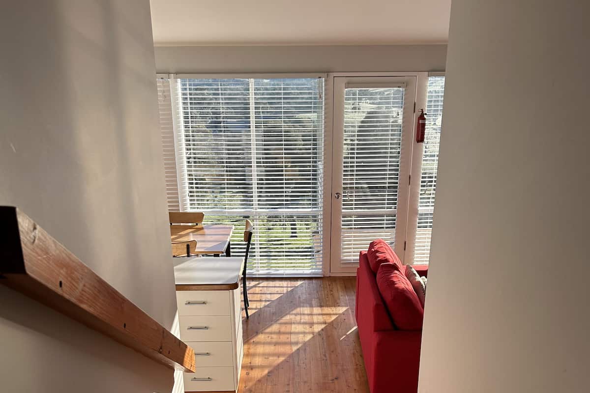 A wooden staircase leading to a room with a red sofa, a small table, and a window with blinds.