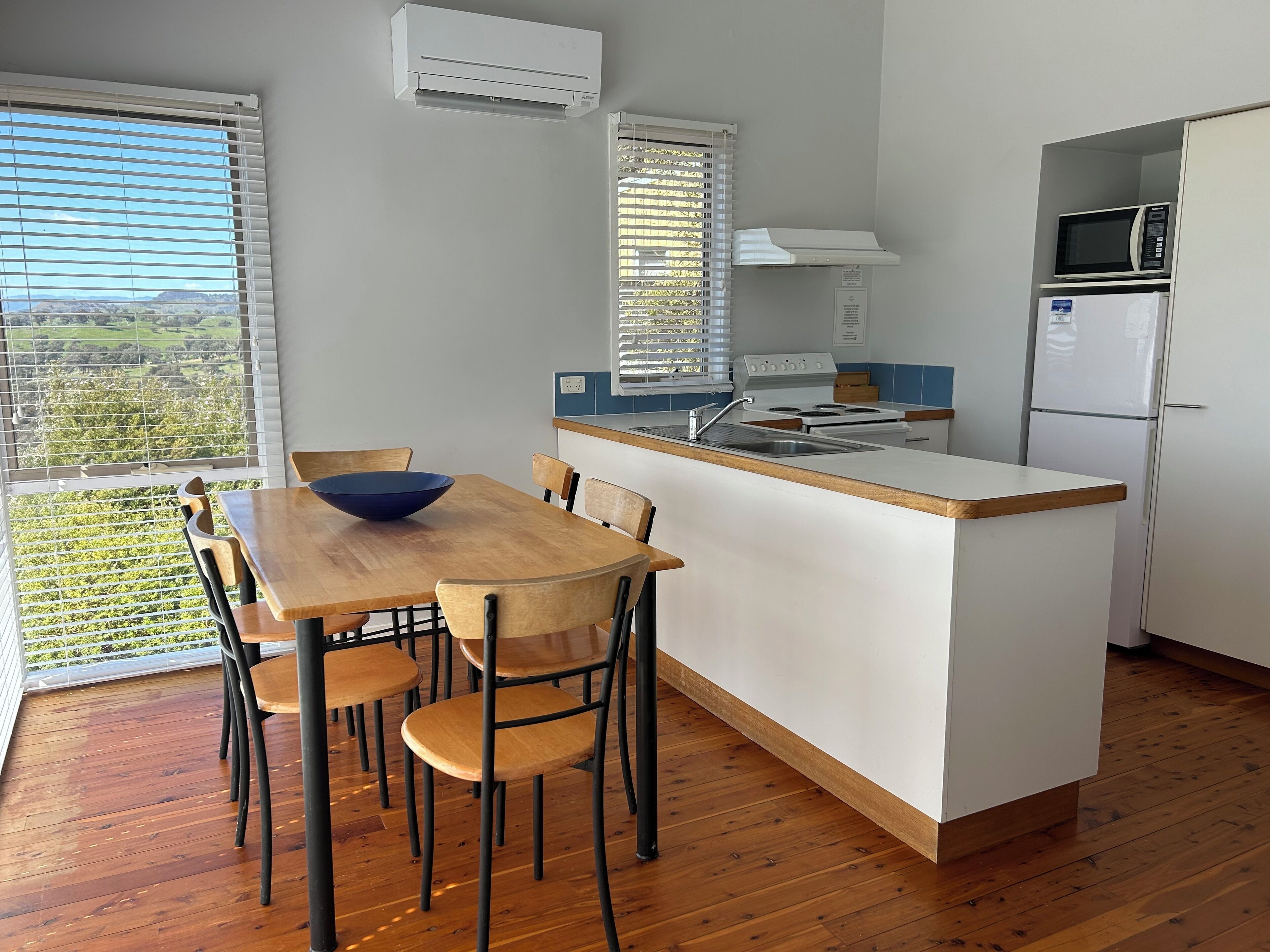 A modern kitchen with a wooden dining table and chairs, a built-in oven, microwave, and refrigerator.