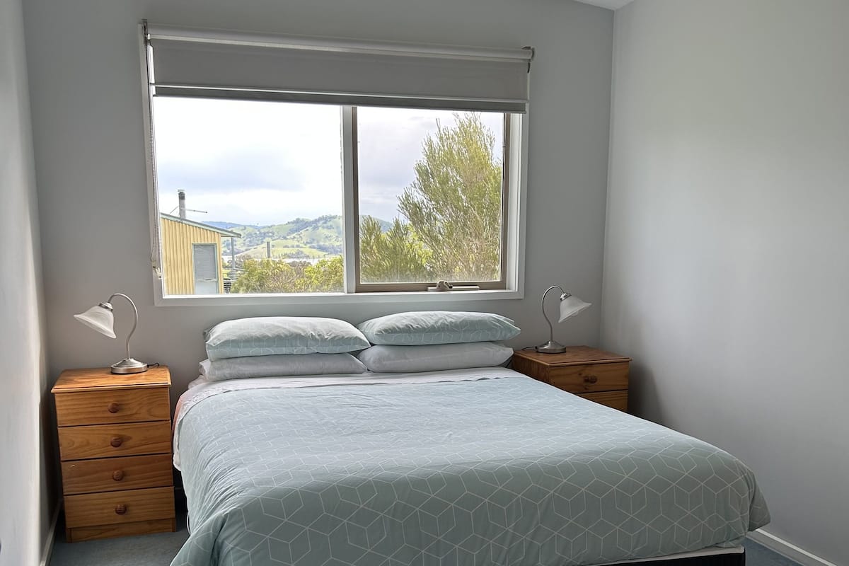 A bedroom with a bed, a window, a ceiling fan, and two bedside tables.