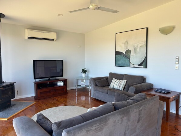 A living room with a flat-screen TV, grey sofas, a coffee table, and a ceiling fan.