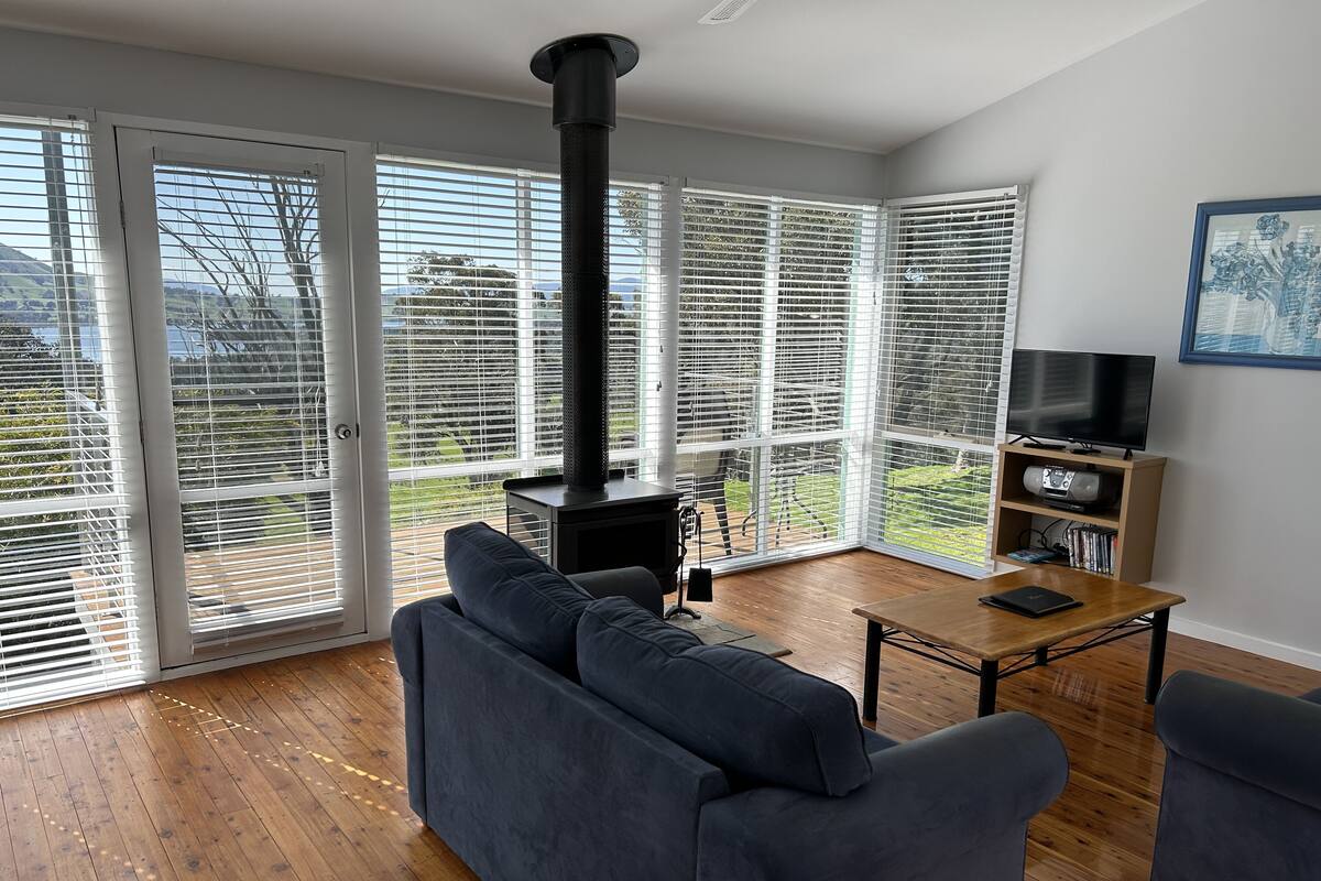 A modern living room with a black wood-burning stove, a grey sofa, a wooden coffee table, and a TV stand with a flat-screen TV and a bookshelf.