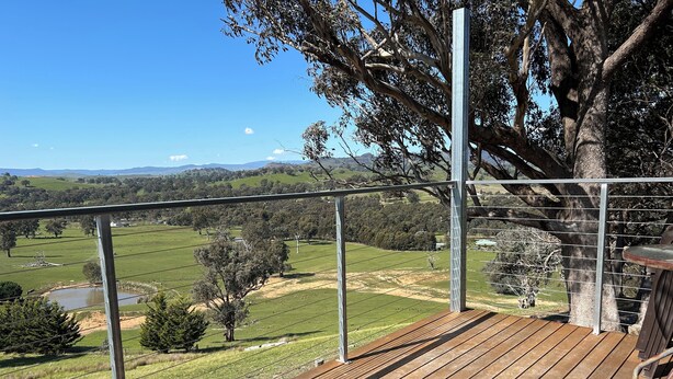 A wooden deck with a metal railing overlooking a rural landscape with fields and trees. - Burnt Creek Cottages Mansfield (Mansfield)