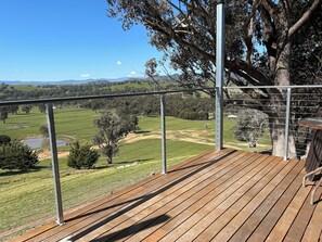 A wooden deck with a metal railing overlooking a rural landscape with fields and trees.