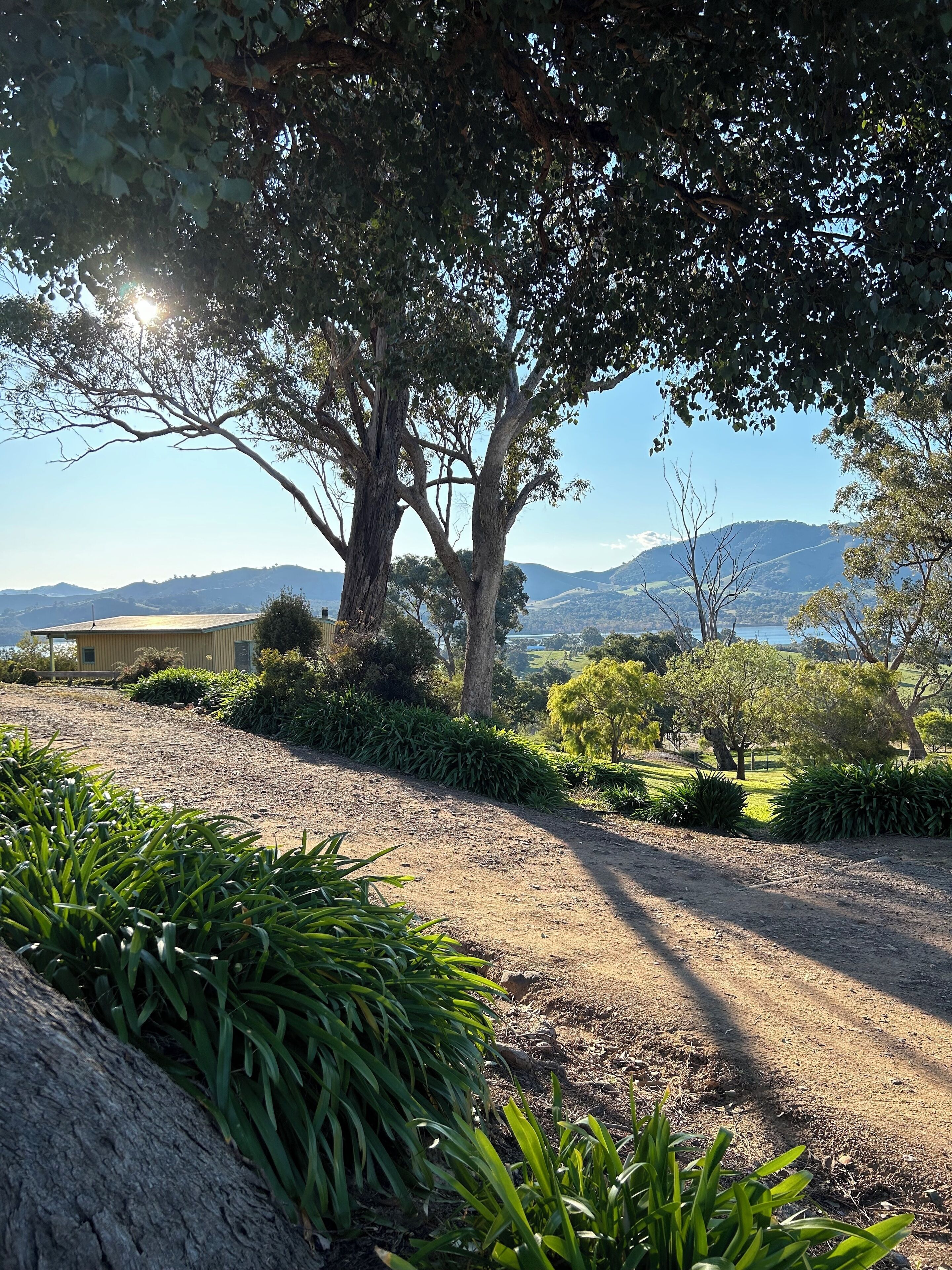 A gravel path leading to a building with a view of distant hills and a body of water.
