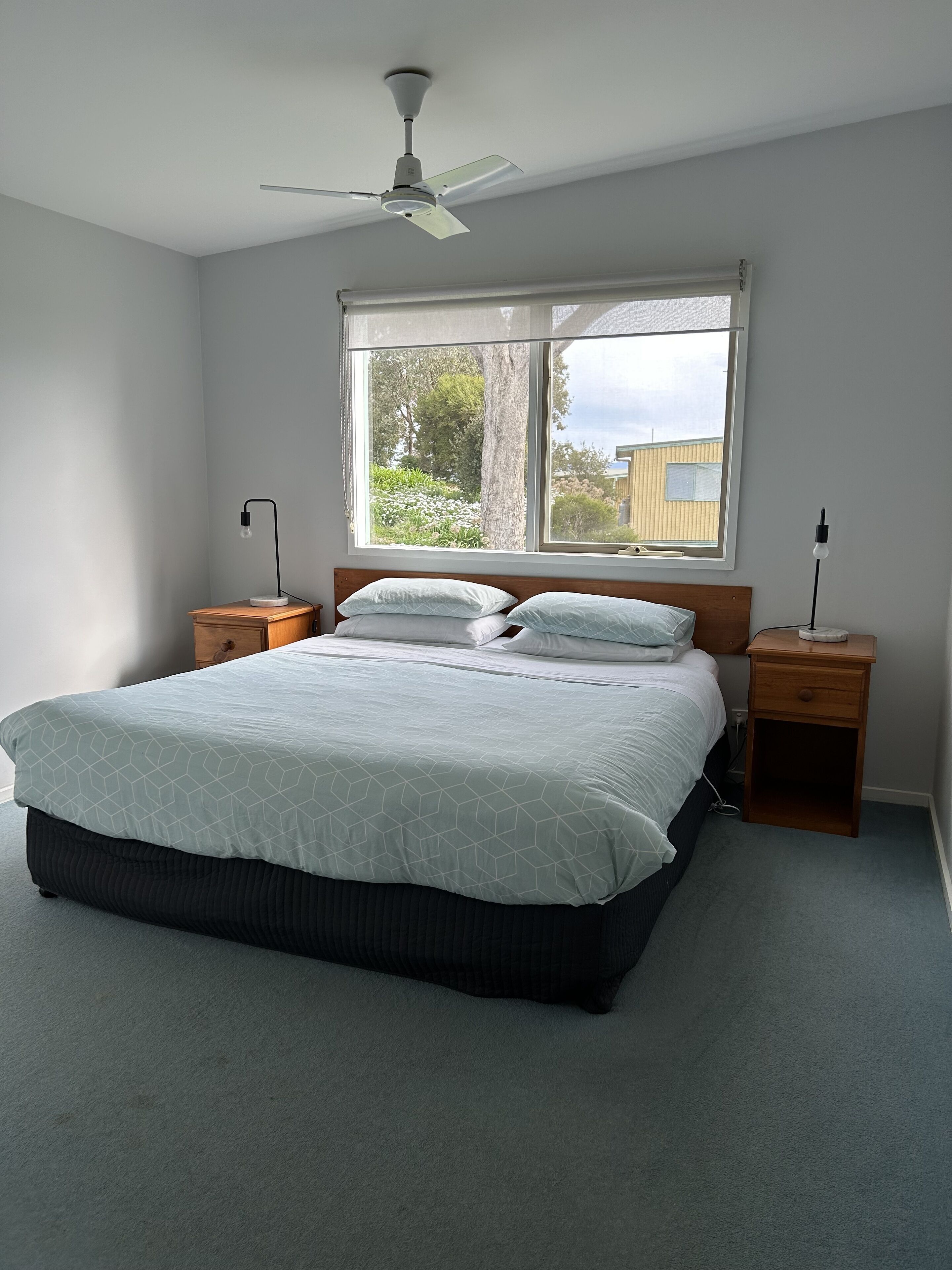 A bedroom with a bed, a ceiling fan, a window, and bedside tables.