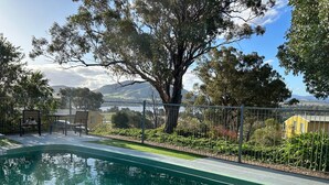 A swimming pool with a metal fence, surrounded by greenery and a view of distant hills. - Burnt Creek Cottages Mansfield (Mansfield)